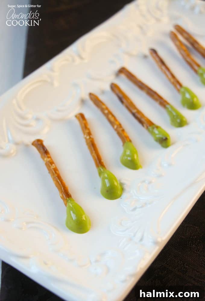 Pretzel sticks with green cheese whiz dipped on one end, ready to be served as a gross Halloween snack.