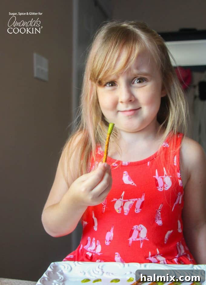 A little girl holding a booger on a stick with a playful expression, showcasing the fun of this Halloween snack.