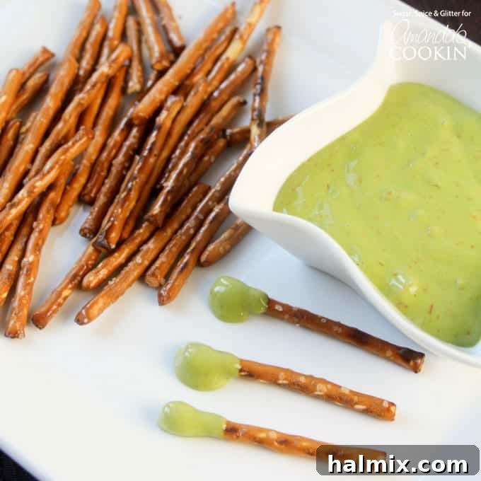 A plate arranged with crisp pretzel sticks, a bowl of vibrant green 'boogers' (cheese dip), and several 'boogers on a stick' ready for a Halloween party.