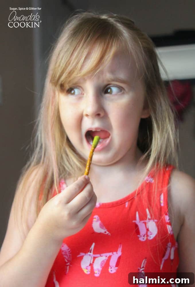 A little girl playfully eating a pretzel, illustrating the fun and surprising deliciousness of the Boogers on a Stick Halloween snack.