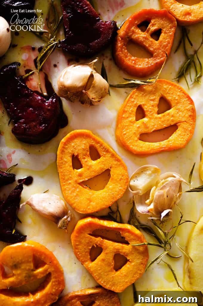A close up overhead photo of roasted Halloween vegetables, showcasing carved sweet potato jack-o-lanterns, potato ghosts, and beet witch hats.