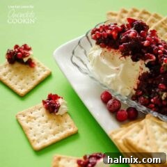 Cranberry salsa spooned over cream cheese in a glass dish with cracker squares surrounding.