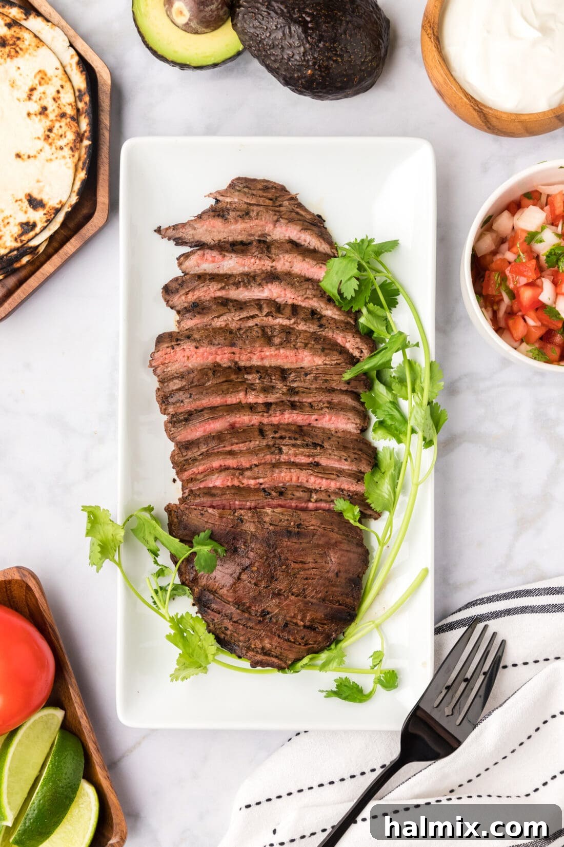 Cooked marinated Carne Asada on a platter with salsa, sour cream and tortillas on the side