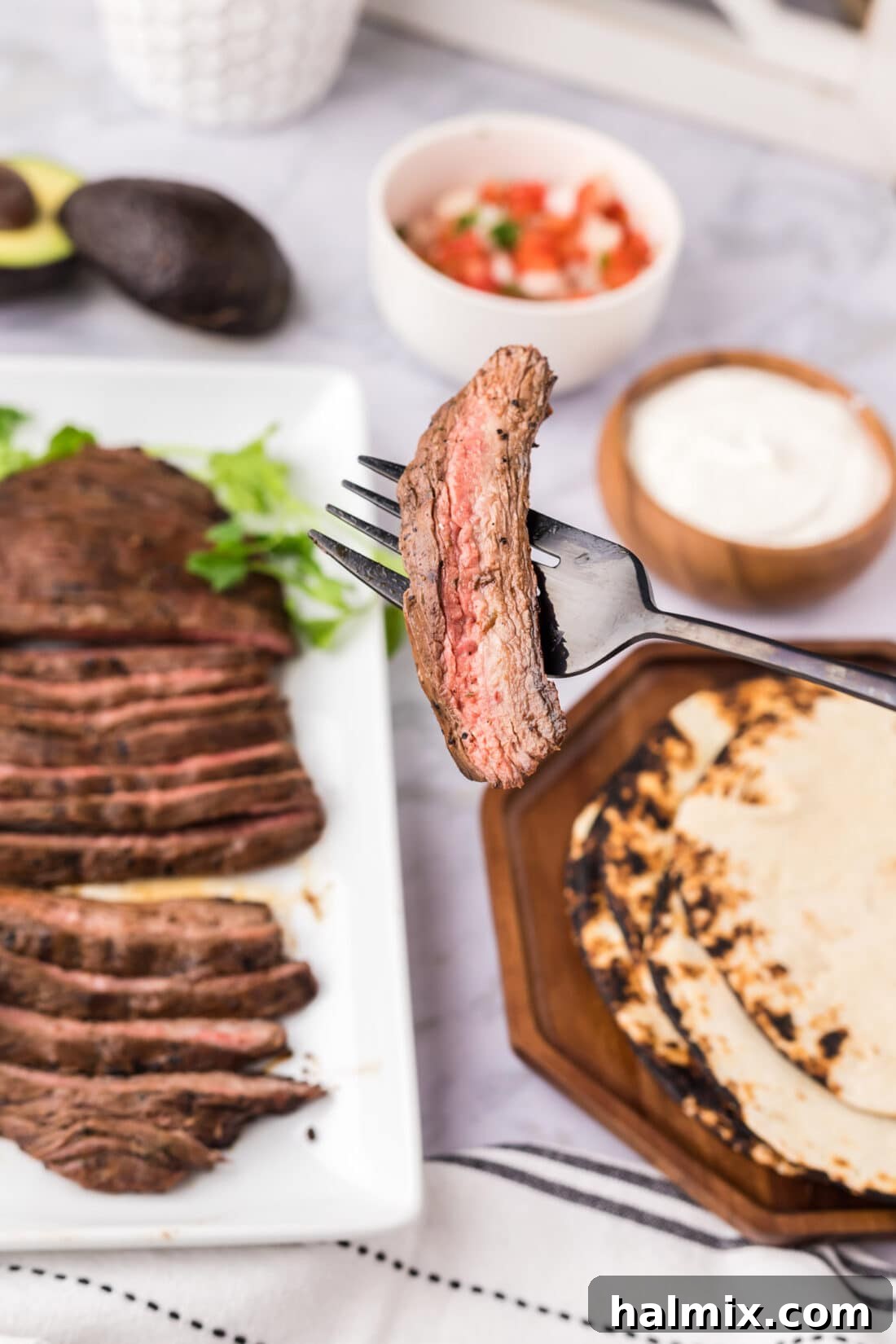 Piece of Carne Asada on a fork with carne asada in the background and other toppings
