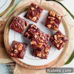 An overhead view of chocolate walnut fudge squares on a white and gold plate.