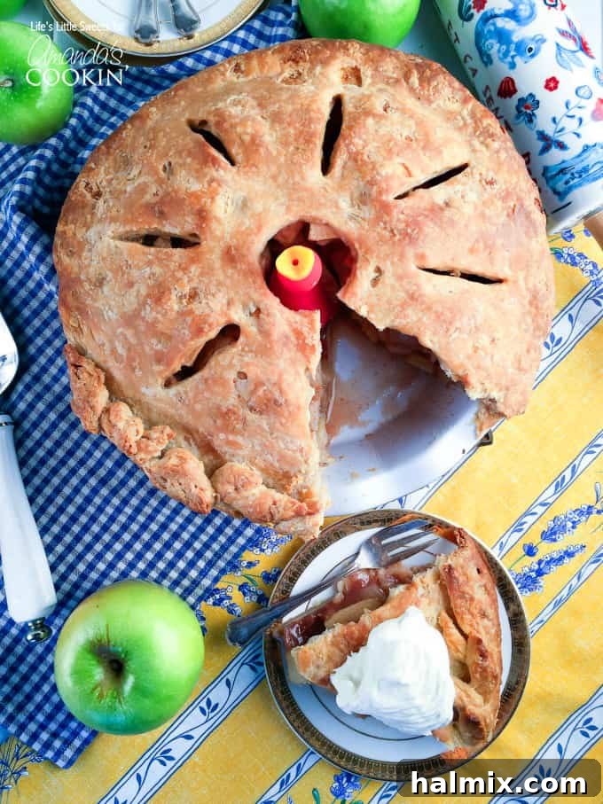 A whole homemade apple pie with a missing slice that is sitting on a plate to the side, revealing the baked apples inside.