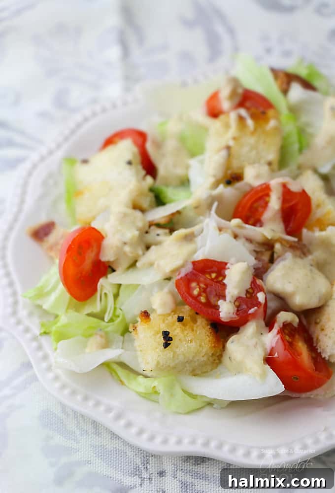 A close up of a vibrant Tomato Caesar Salad on a white plate, showcasing fresh lettuce, cherry tomatoes, and creamy dressing.