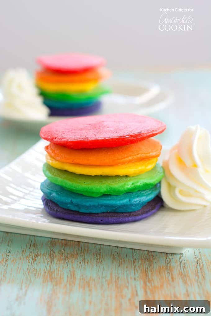 Stacked rainbow pancakes for St. Patrick's Day breakfast, or for a fun, colorful treat, topped with fluffy whipped cream clouds.