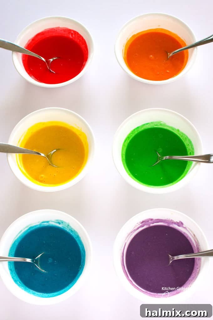 Six small bowls filled with pancake batter, each dyed a different vibrant rainbow color: red, orange, yellow, green, blue, and purple.