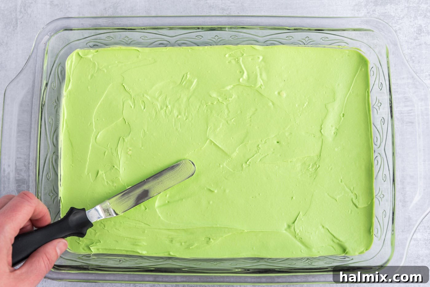 Invigorating Mint Chocolate Lasagna 9 An icing spatula spreading the green cream cheese mixture evenly over the Oreo crust in a pan