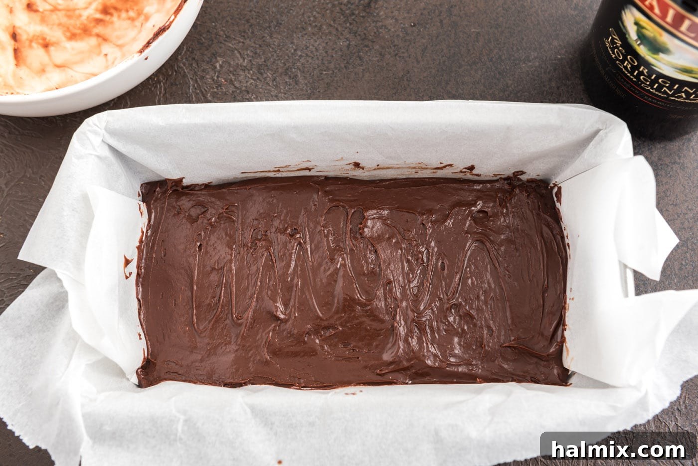 The smooth chocolate fudge mixture being spread into a parchment-lined loaf pan.