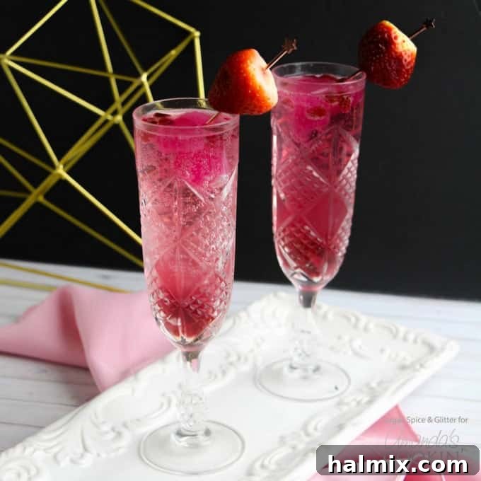 Two pink Cupid's Cocktails in champagne flutes, garnished with strawberries and pomegranate seeds.