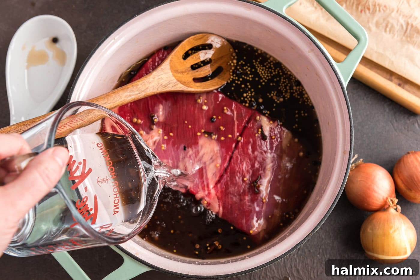 pouring water over beef brisket in a Dutch oven