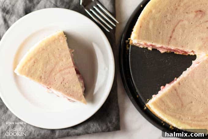 Velvet Strawberry Swirl Cheesecake 5 A beautiful slice of strawberry swirled cheesecake on a white plate, presented alongside the whole baked cheesecake.