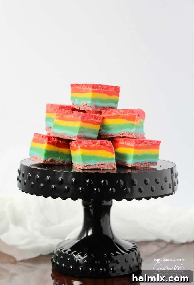 Cubes of rainbow fudge stacked up on a black cake stand, showcasing vibrant layers of color.