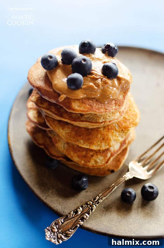 Grain-Free Banana Breakfast Cakes 2 A beautiful stack of golden-brown flourless banana pancakes, topped with fresh blueberries, resting on a rustic brown plate, ready to be enjoyed.