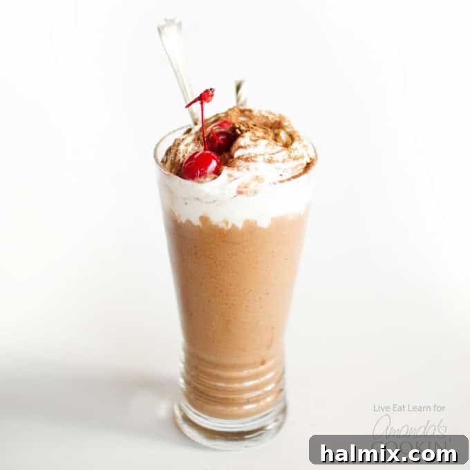 A close-up shot of a dark, rich chocolate nice cream milkshake, topped with a dollop of whipped cream and a bright red maraschino cherry, ready to be enjoyed.