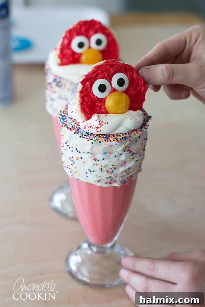 Two vibrant Elmo Freakshakes, garnished with whipped cream and Elmo cookies, presented as a finished dessert ready to be enjoyed.