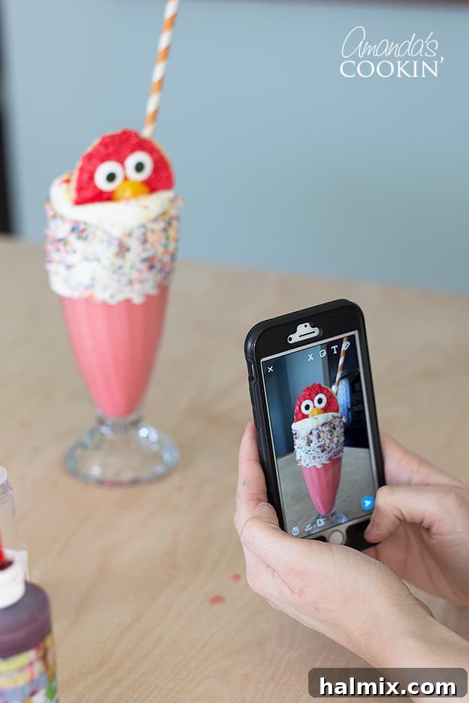 A person taking a picture of an Elmo Freakshake with a smartphone, highlighting its visually appealing and shareable nature.