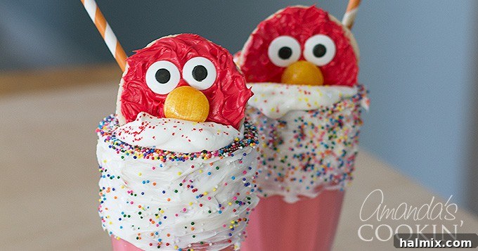 A close-up of a beautifully decorated Elmo cookie resting on a mound of whipped cream atop a red milkshake, showcasing the irresistible charm of Elmo Freakshakes.