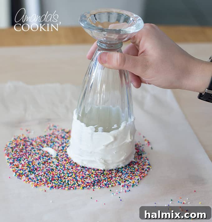 A milkshake glass being inverted and dipped into a pile of colorful sprinkles on a flat surface, illustrating the glass decorating technique.