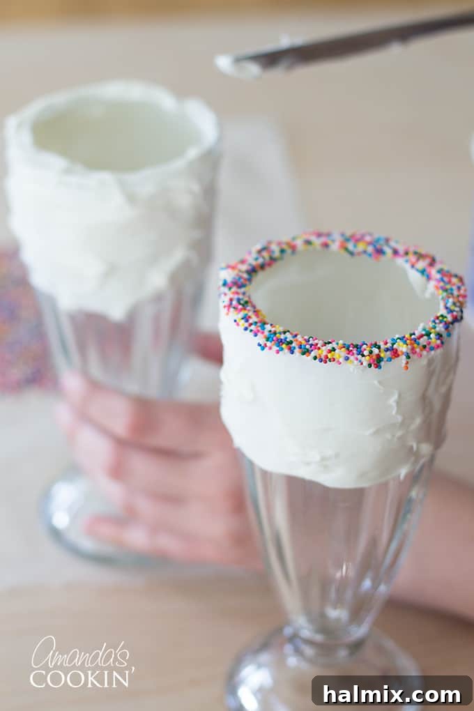 A close-up of a milkshake glass rim fully coated in bright, multi-colored sprinkles, ready for the next step in creating an Elmo Freakshake.