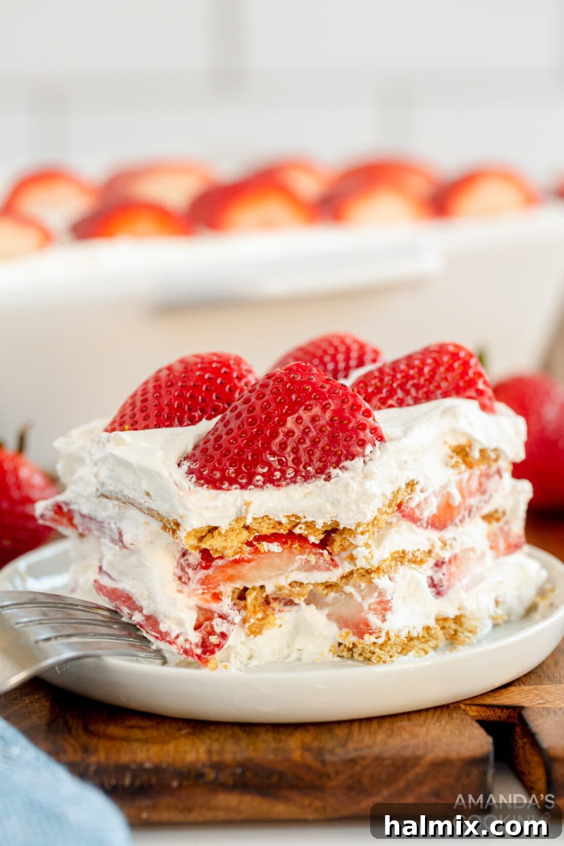 Slice of Strawberry Icebox Cake showing layers of whipped cream, graham crackers, and fresh strawberries.