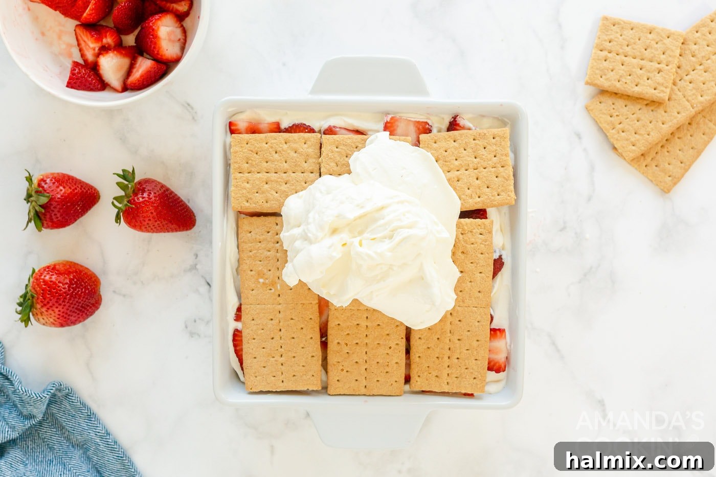 Whipped cream spread over a layer of graham crackers and strawberries, ready for the final touches.