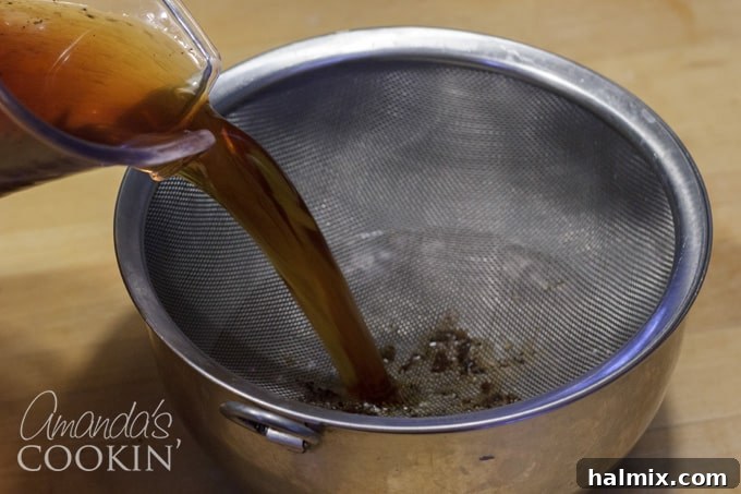 Refreshingly Smooth Cold Brew 6 Pouring steeped coffee through a fine mesh strainer into a clean bowl, the initial step in separating grounds from liquid.