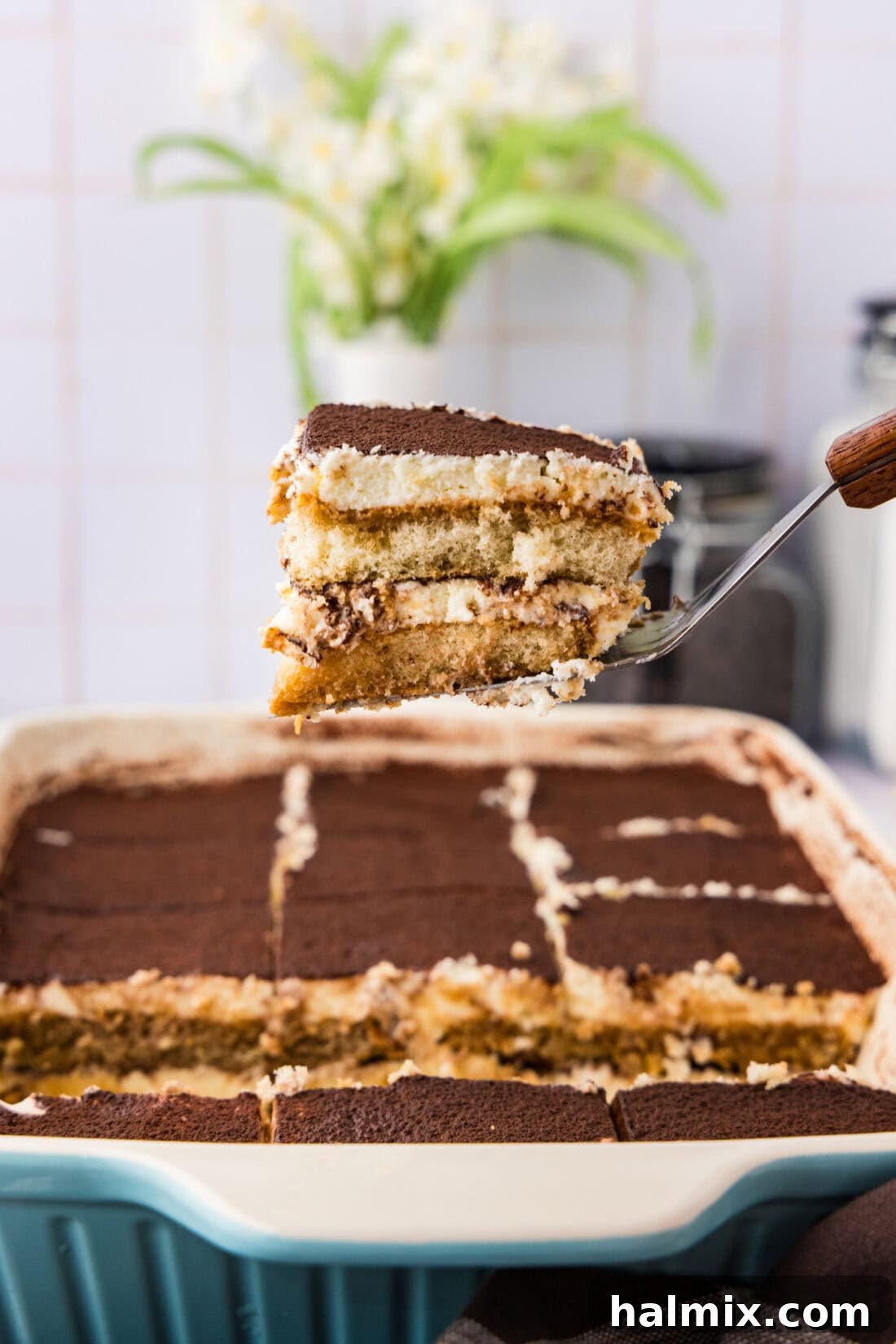 A slice of Tiramisu Icebox Cake being carefully lifted from a 13x9 baking dish, showcasing its perfect layers and smooth cream.