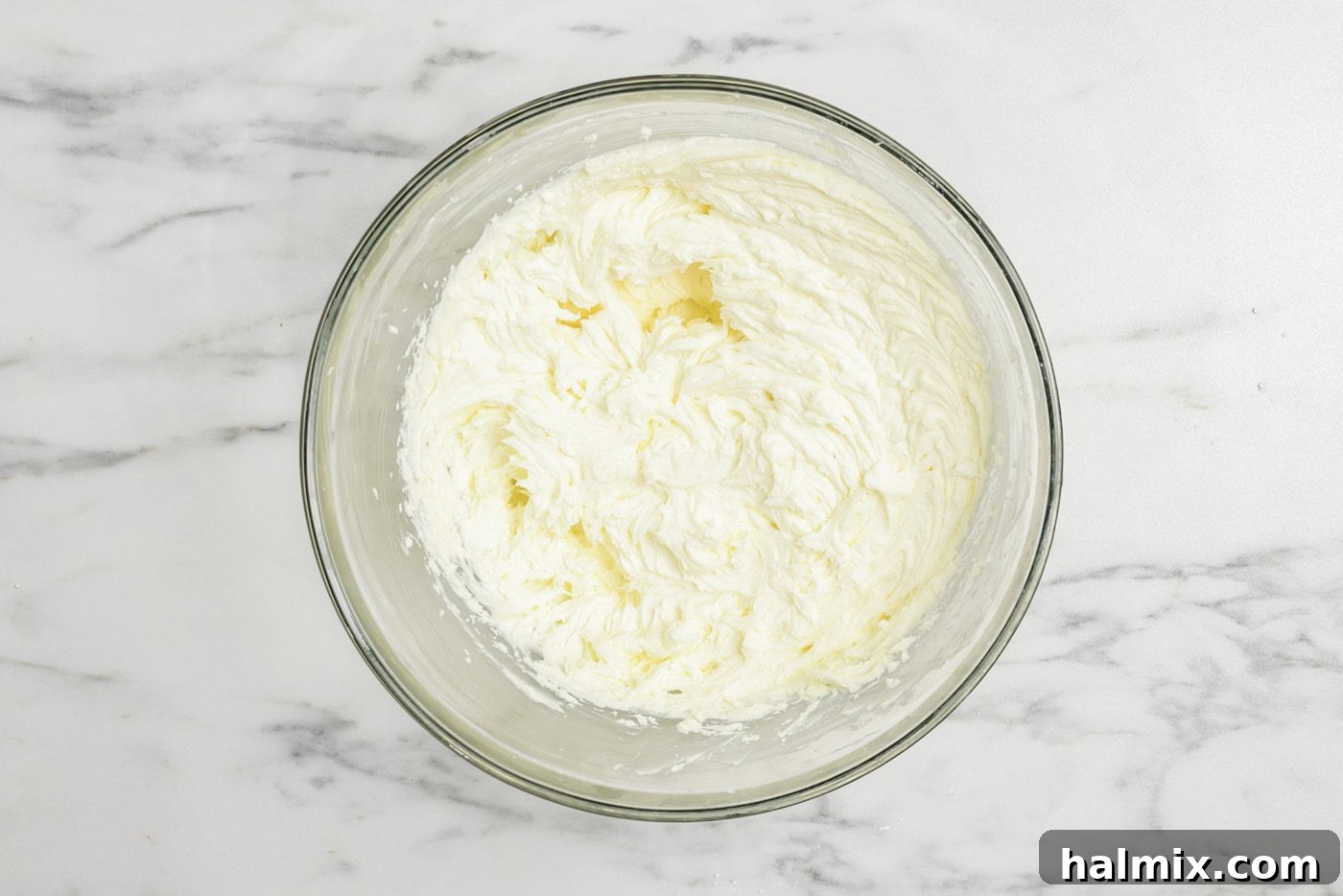 Cream cheese, mascarpone cheese, and powdered sugar are being mixed together in a large bowl with an electric mixer, forming a smooth, creamy base for the tiramisu filling.