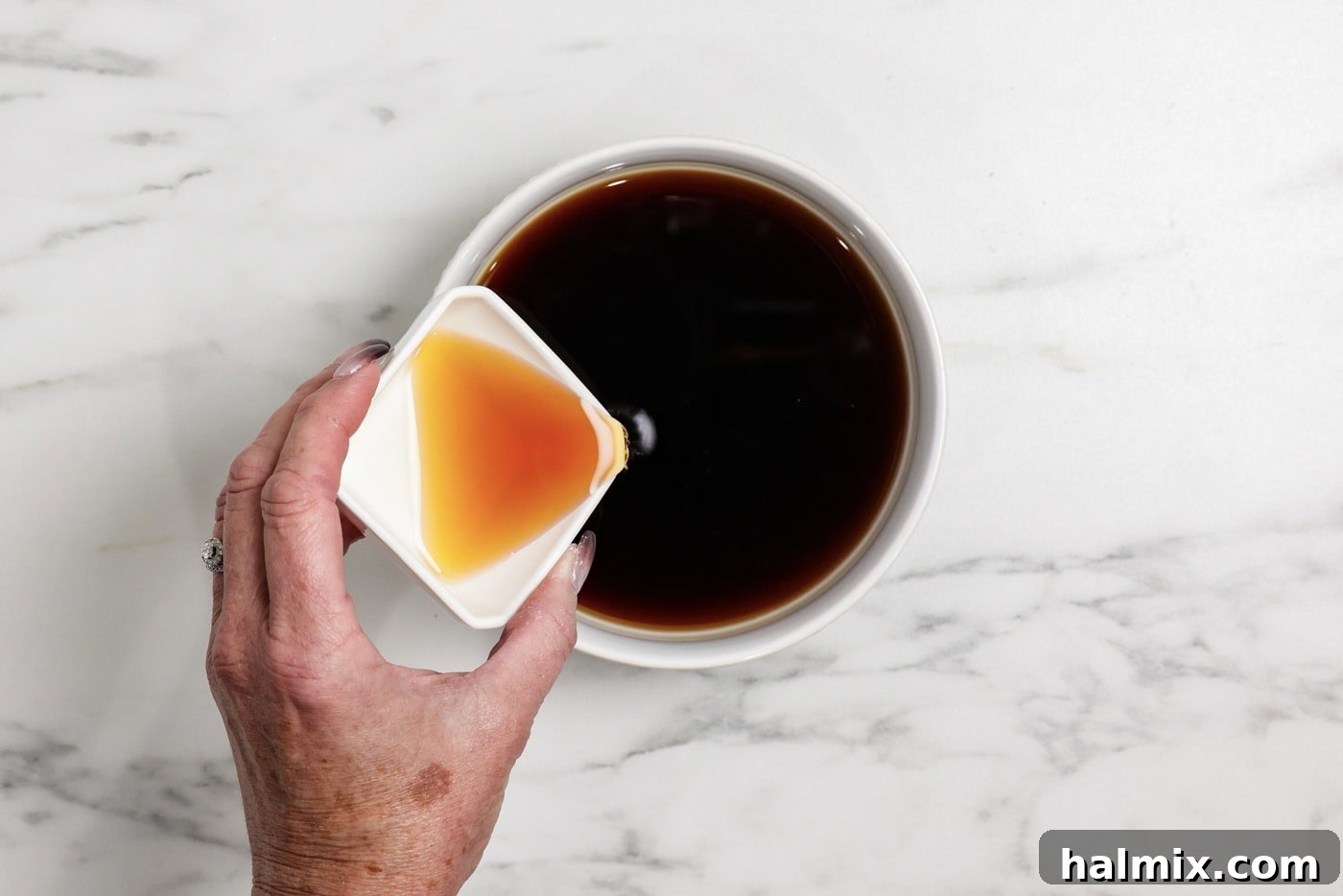 Amaretto liqueur is being poured into a bowl of cooled instant espresso, preparing the flavorful soaking liquid for the ladyfingers.