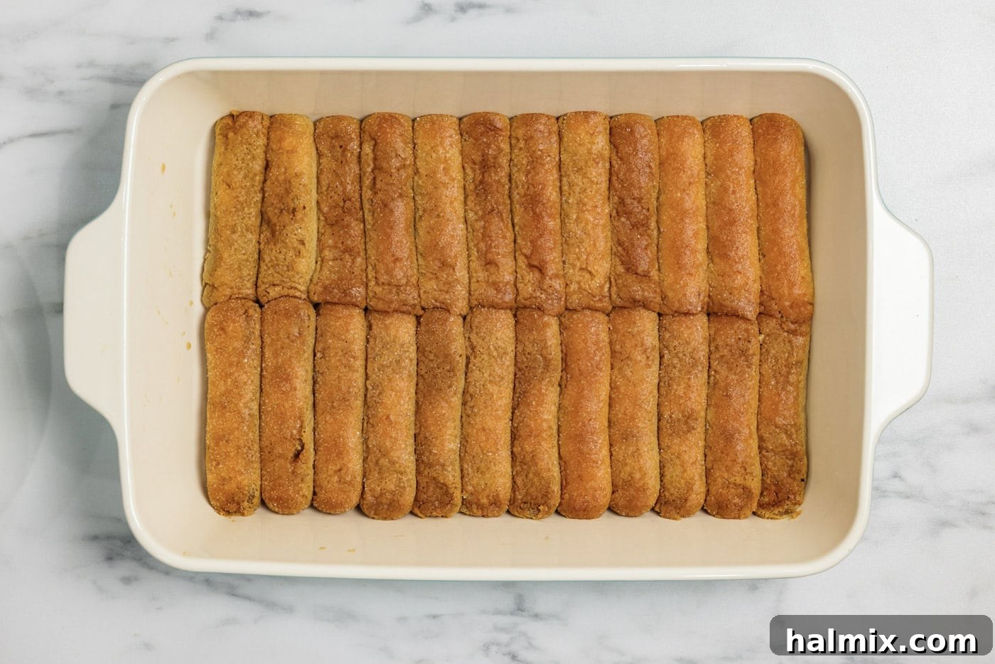 The first layer of espresso-dipped ladyfingers is neatly arranged at the bottom of a 13x9 inch baking dish, ready for the creamy filling.