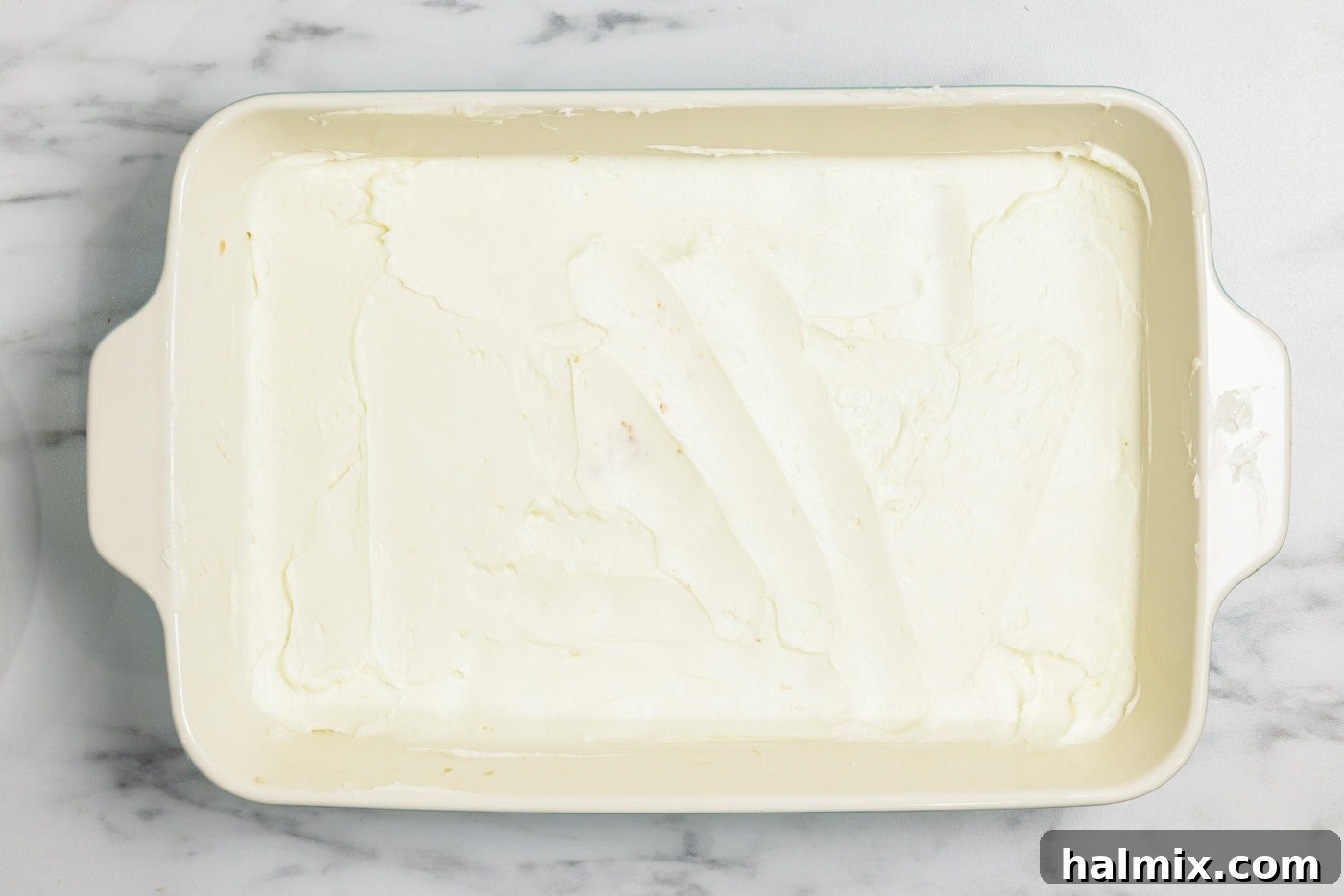 Half of the creamy mascarpone mixture is spread evenly over the first layer of espresso-soaked ladyfingers in the baking dish.