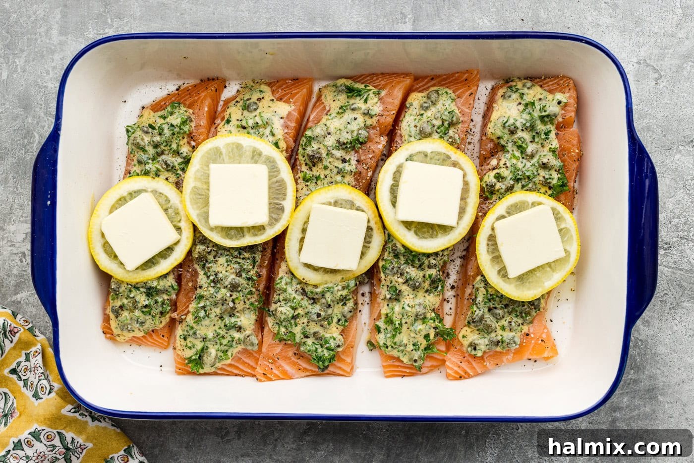 butt pats placed on top of lemon slices over raw lemon caper salmon in a dish