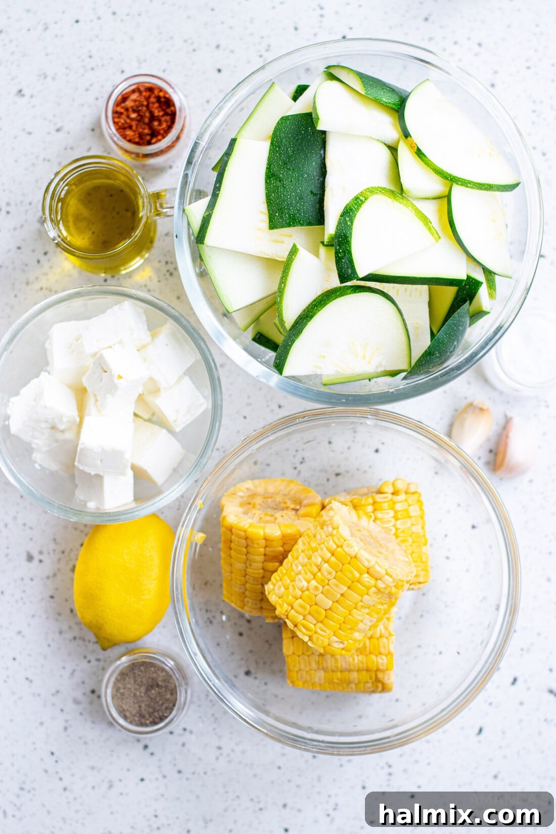 Fresh ingredients for Grilled Corn & Zucchini Salad with Feta laid out on a cutting board, including corn, zucchini, feta, lemon, and spices