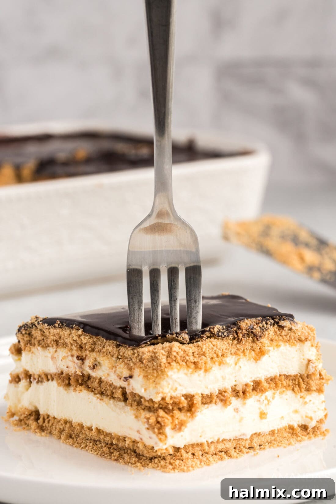 A fork plunged into a perfectly sliced piece of Eclair Cake, revealing its luscious layers of graham cracker, creamy filling, and rich chocolate ganache.