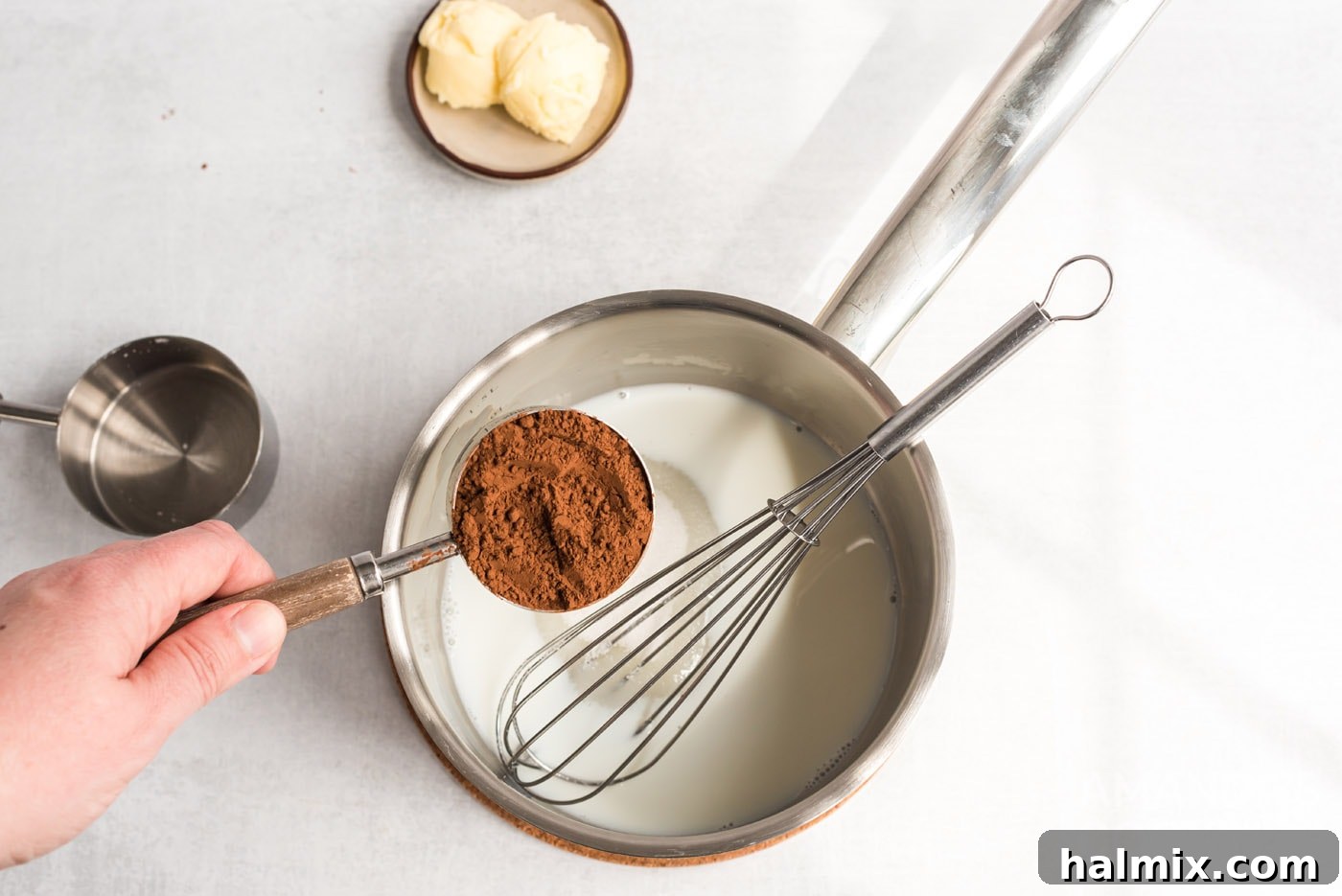 Sifted cocoa powder and sugar being added to warmed milk in a small saucepan on the stove for the ganache.