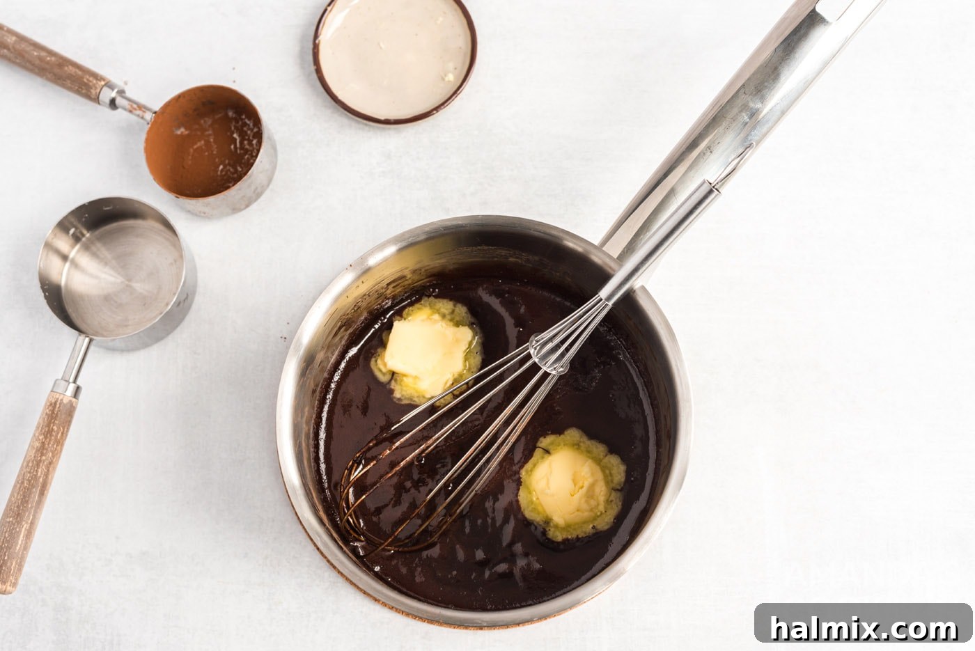 Whisking softened butter into the hot chocolate ganache mixture in the saucepan until smooth and glossy.