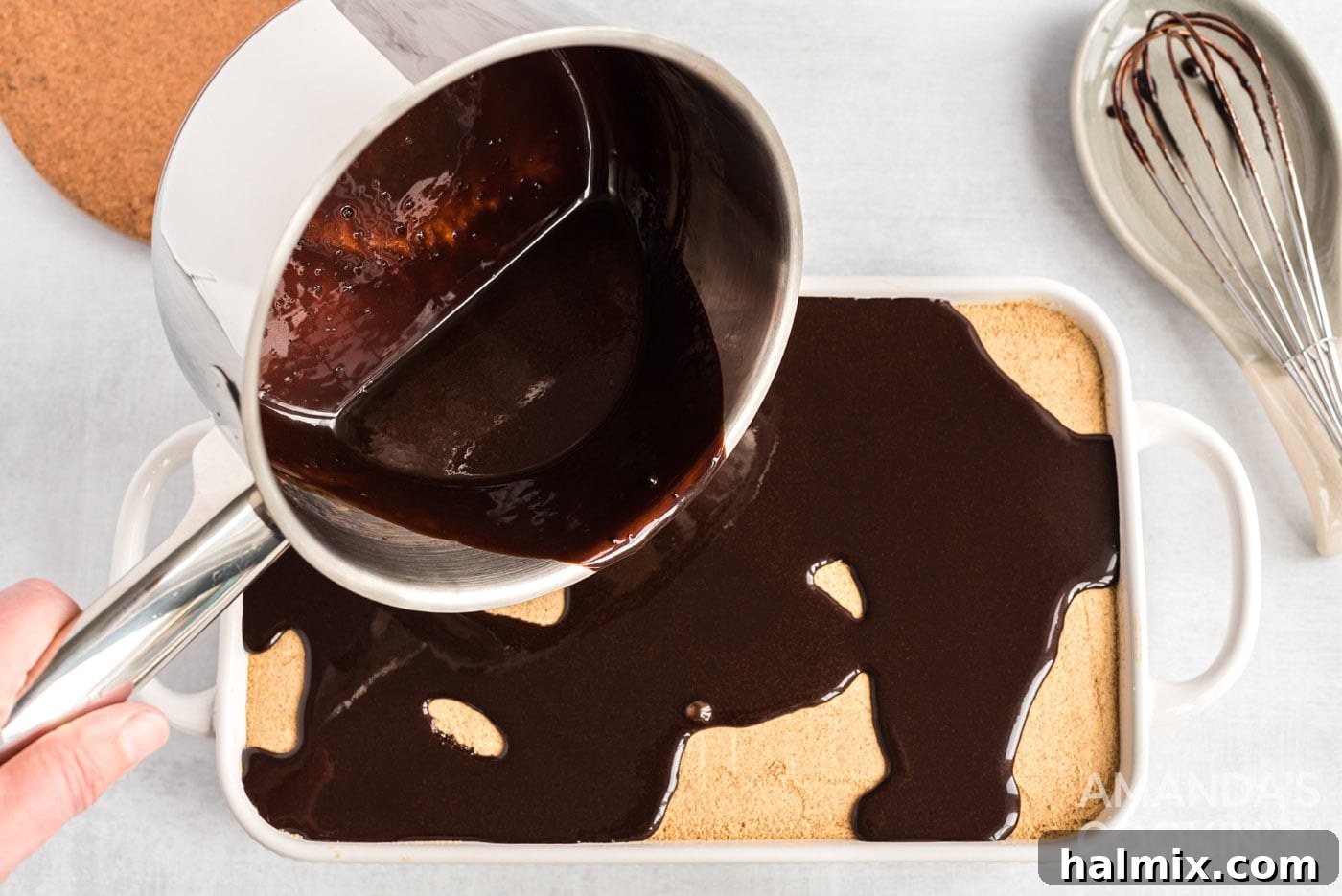 Pouring rich chocolate ganache over the top of the layered eclair cake in the baking dish.
