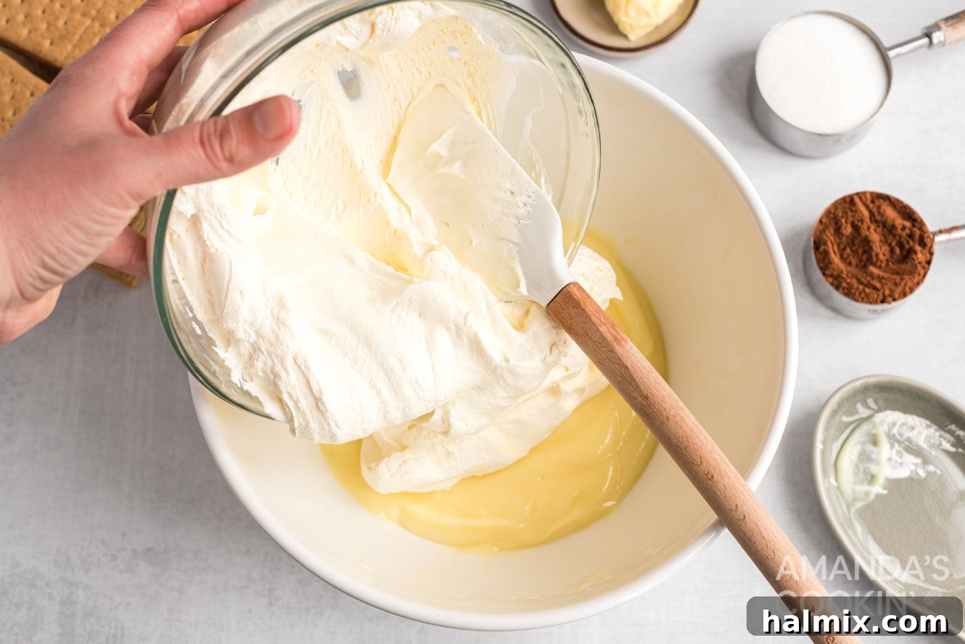 Adding a scoop of whipped topping to the prepared pudding mixture in a bowl, preparing to fold.