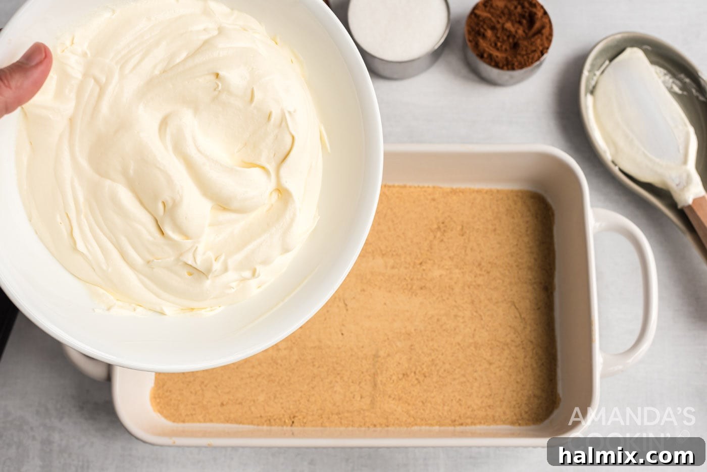 Half of the creamy pudding mixture being poured over the first layer of graham crackers in the baking dish for the eclair cake.