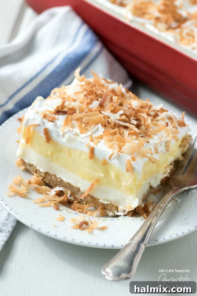 A perfectly sliced piece of Coconut Cream Lush, showcasing its beautiful, distinct creamy layers and a sprinkle of toasted coconut on top.