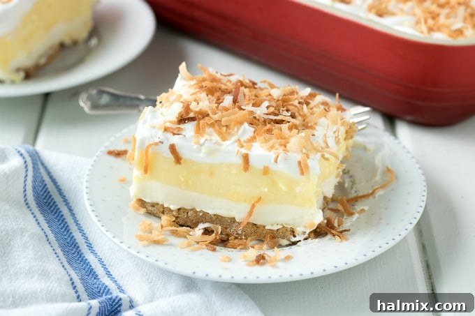 A single, perfectly portioned slice of Coconut Cream Lush rests on a pristine white plate, inviting dessert enthusiasts to savor its delightful layers.