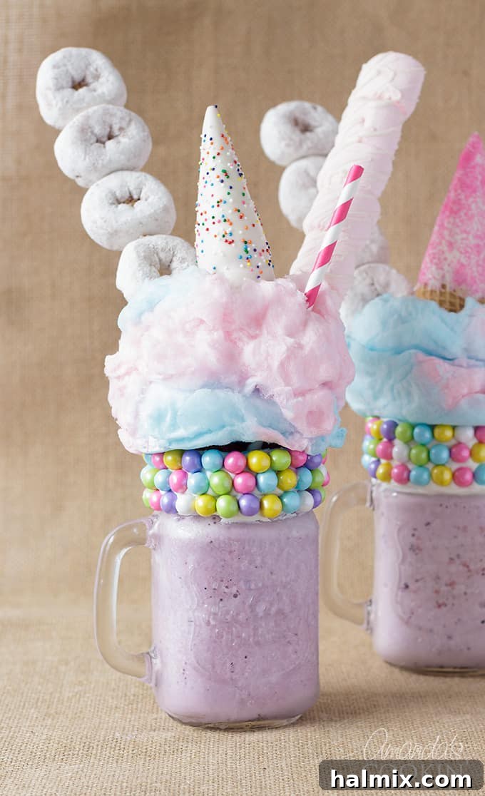 Two vibrant purple unicorn freakshakes, generously topped with mini donuts, fluffy cotton candy, and colorful marshmallows, set against a whimsical backdrop.