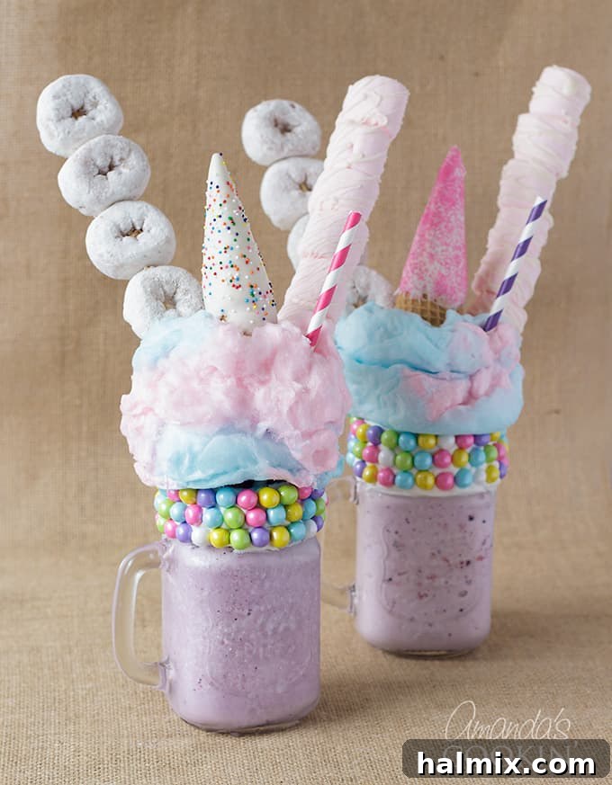 Close-up of two beautifully crafted purple unicorn freakshakes, adorned with mini powdered donuts, soft marshmallows, and whimsical cotton candy, ready to be enjoyed.