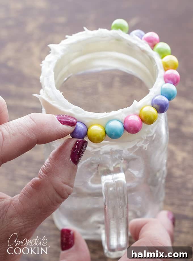 Step 1 in making unicorn freakshakes: A glass rim is generously coated with vanilla frosting, ready for candy pearls, illustrating the preparation of the decorative glass.