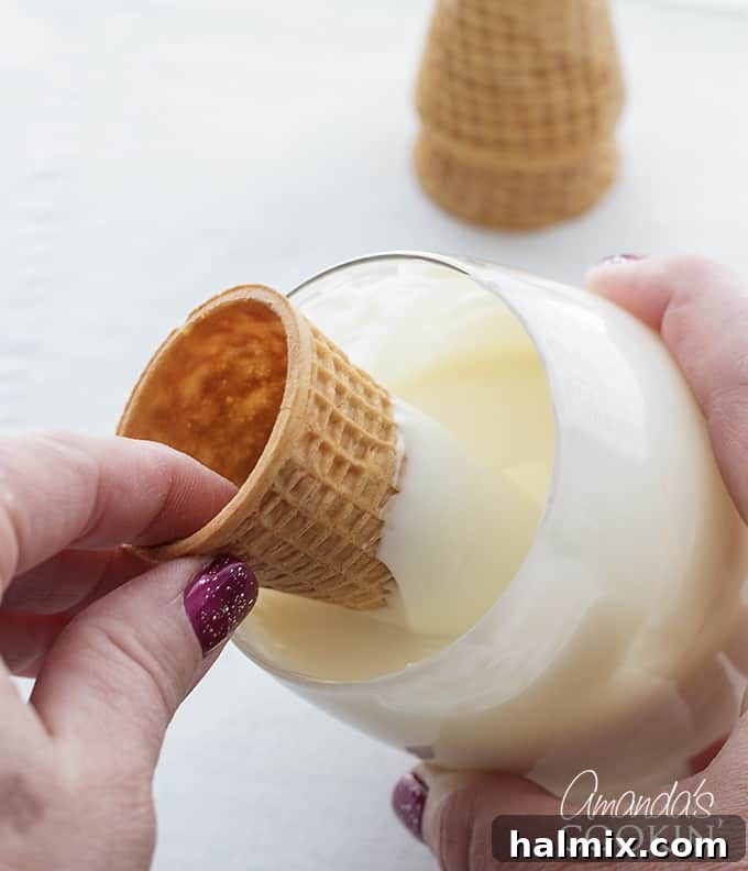 Step 2 in making unicorn freakshakes: Melted white chocolate in a glass, ready for dipping sugar cones to create unicorn horns, showing the start of a key topping.