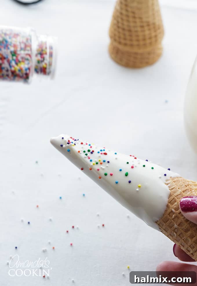 Step 3 in making unicorn freakshakes: A dipped sugar cone adorned with colorful sprinkles while the chocolate is still wet, demonstrating the decorative step for the unicorn horn.