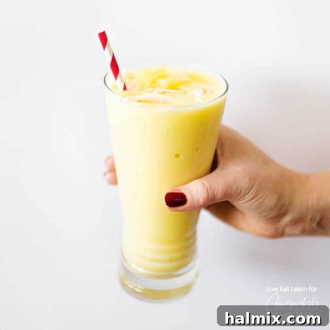 Hand holding a glass of creamy Pina Colada Smoothie garnished with coconut flakes